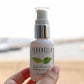 Bottle of Verabella Aloe Hydroxy serum held in a hand at the beach