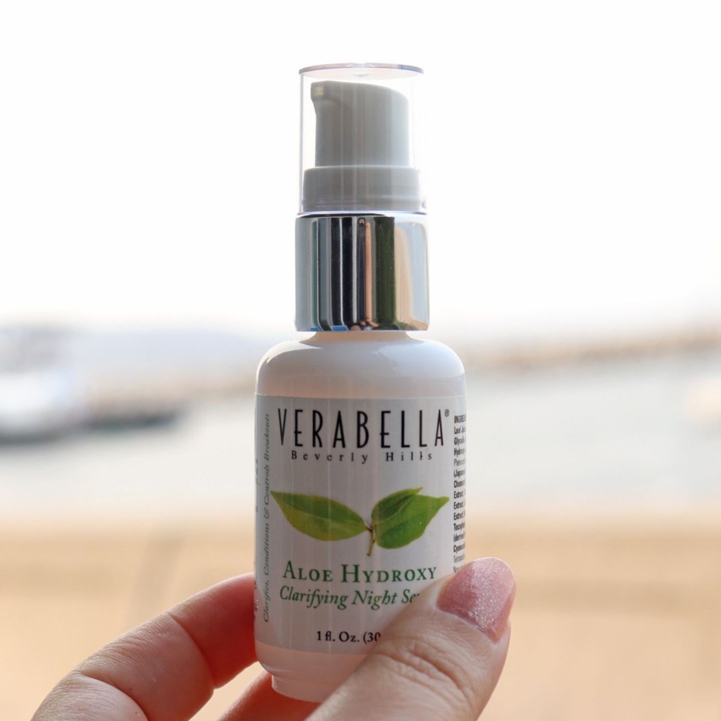 Bottle of Verabella Aloe Hydroxy serum held in a hand at the beach